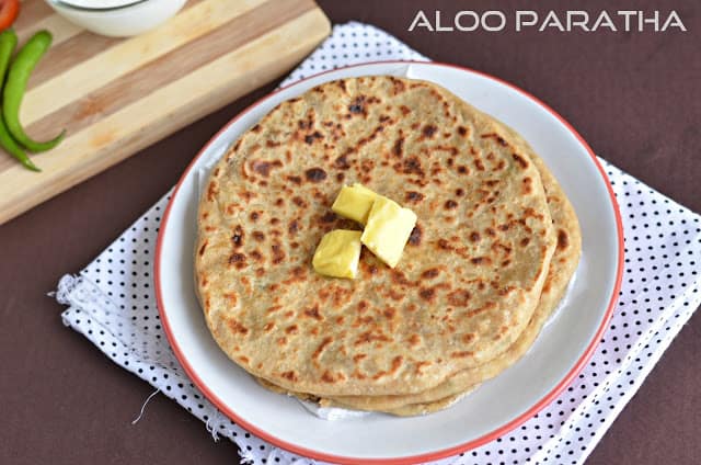 Aloo paratha served with butter in a white plate.