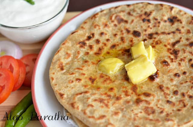 a closeup click of aloo paratha with butter & curd.