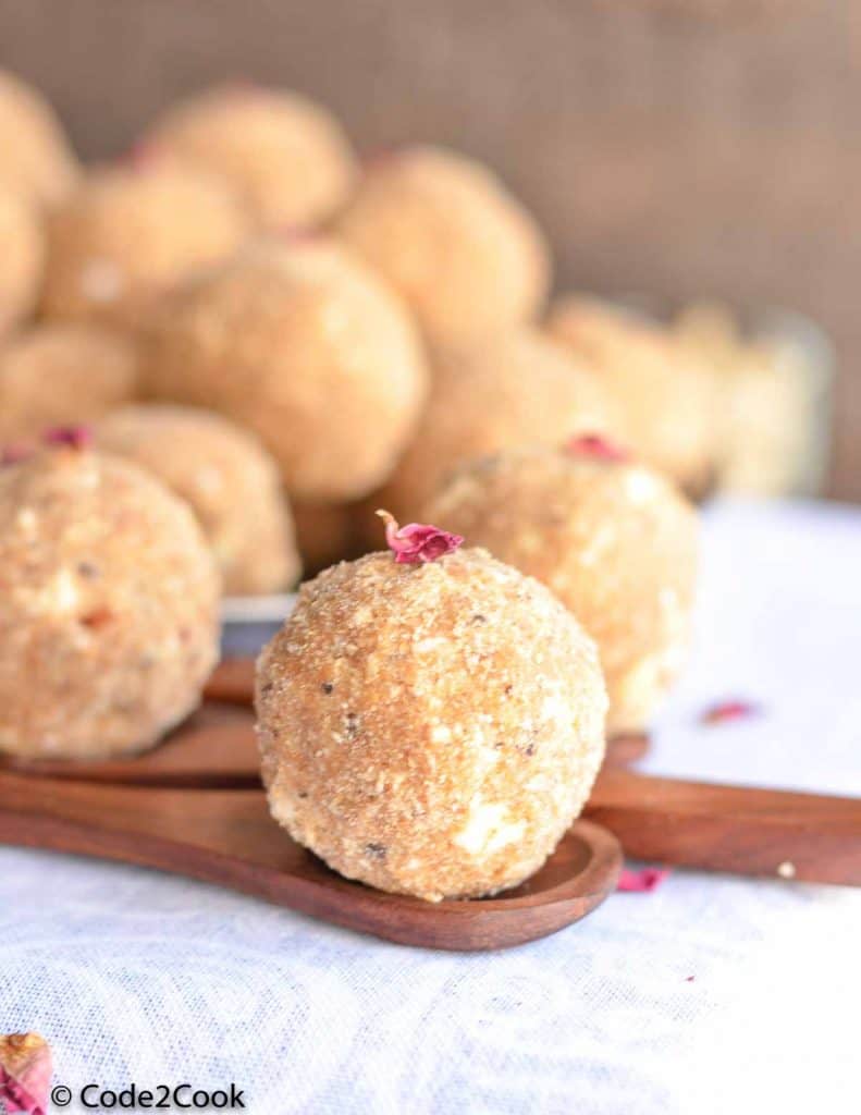 a close up click of gond ladoo kept on wooden spoon.