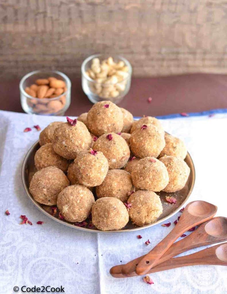 dry fruits laddu with gond & wheat flour are served in a big plate. cashew, almond & wooden spoon placed sidewise
