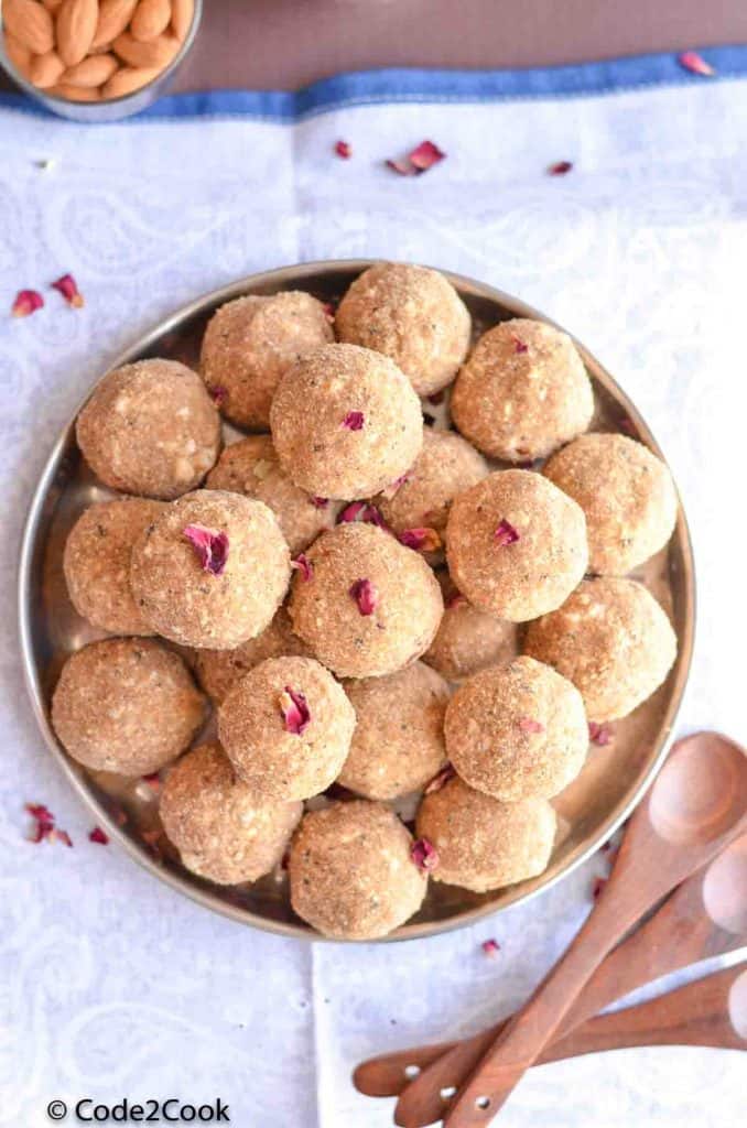 gond ke laddu placed in a big plate with wooden spoons sidewise.