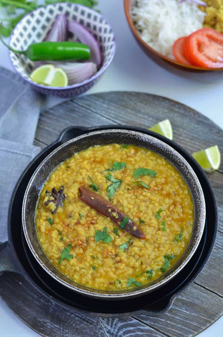 white urad dal tadka served in black bowl with lemon wedges.
