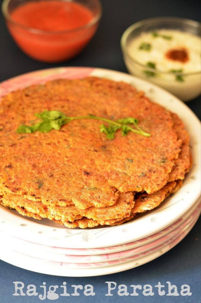 Rajgira Paratha Recipe | Vrat Ka Paratha | Farali Paratha Rajgira paratha with vegetables served in a stack of plates. Coriander leaf is placed over them.