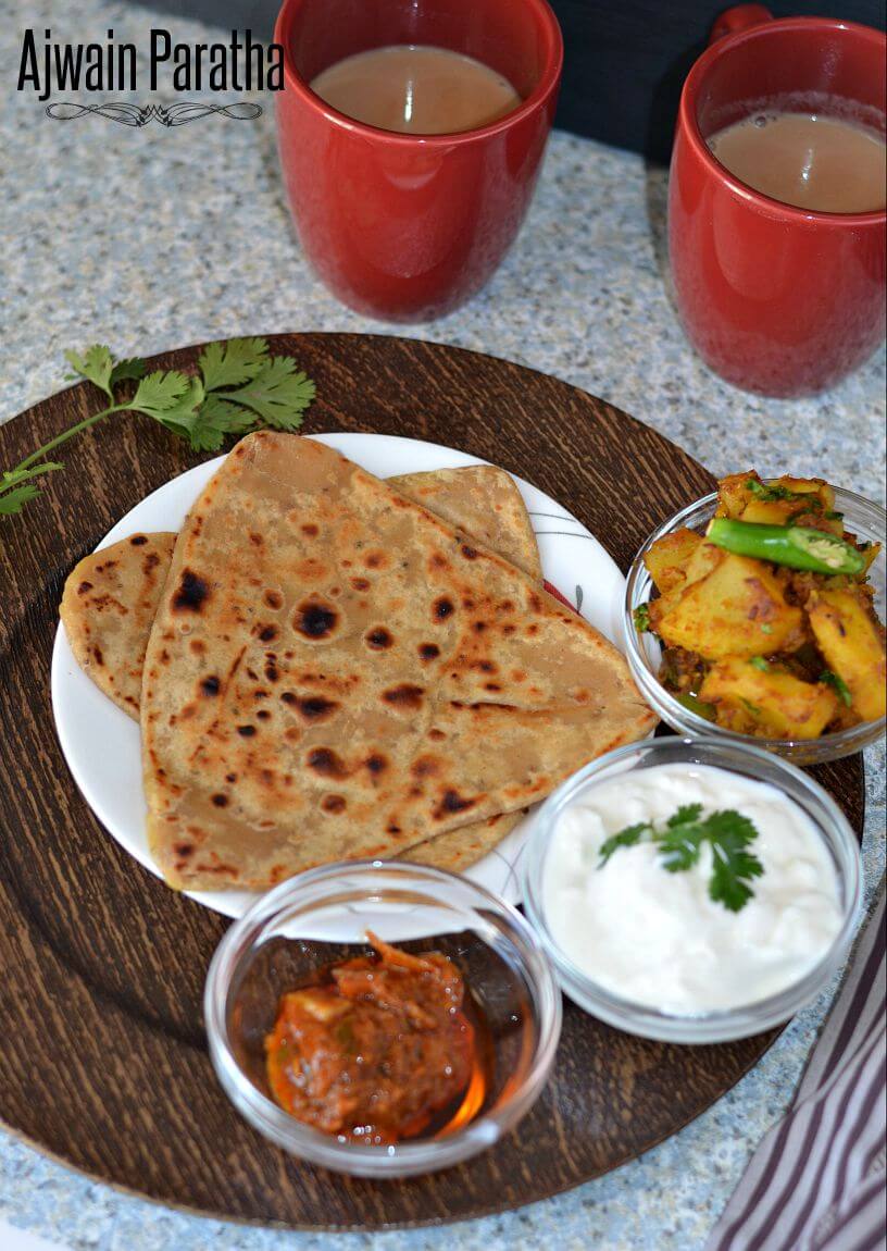 Ajwain ka paratha served with pickle, curd & potato curri. Masala chai cups are alongside.