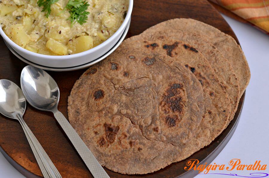 Rajgira Paratha | Amarnath Flour Paratha | Vrat Ka Paratha | Falahari Paratha | GF | V Amarnath flour paratha is served with vrat ke aloo on a wooden board. Spoons are kept around it.