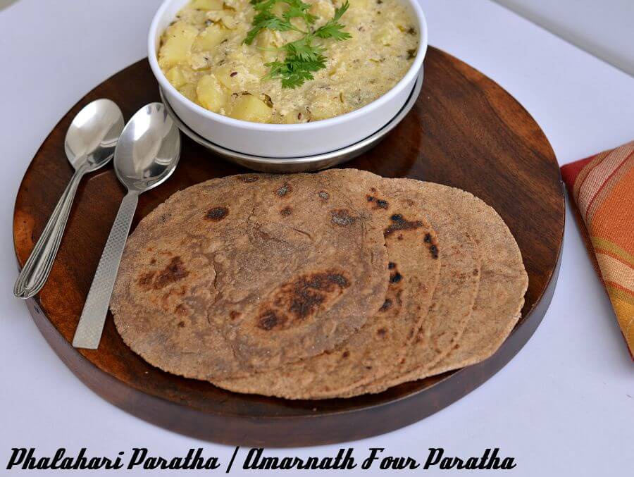Rajgira Paratha | Amarnath Flour Paratha | Vrat Ka Paratha | Falahari Paratha | GF | V Amarnath flour paratha is served with vrat ke dahi aloo on a wooden boards. Sppons are kept on one side.