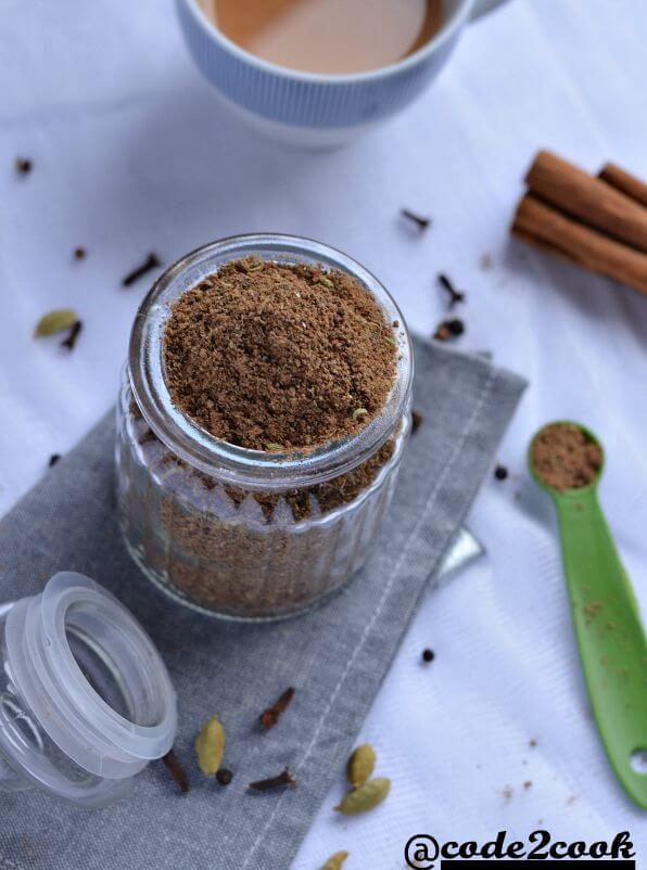 homemade masala chai spice mix is shown in glass jar, surrounded by whole spices. Photo is taken from top.