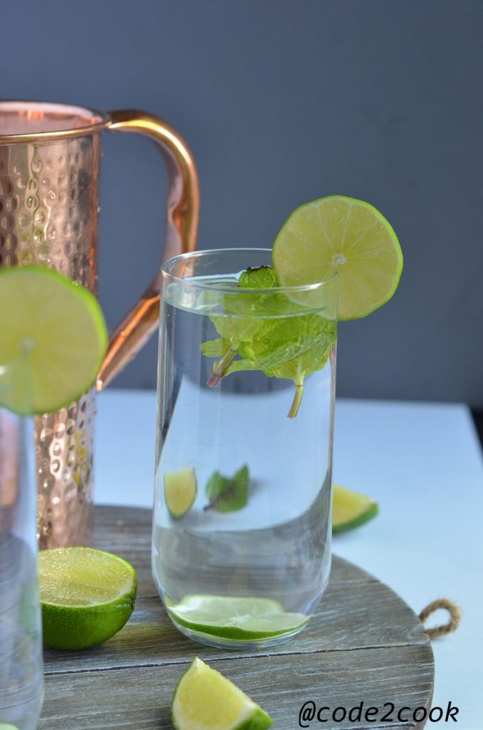 copper enriched water poured in a glass. mint leaves and lemon wedges are added.