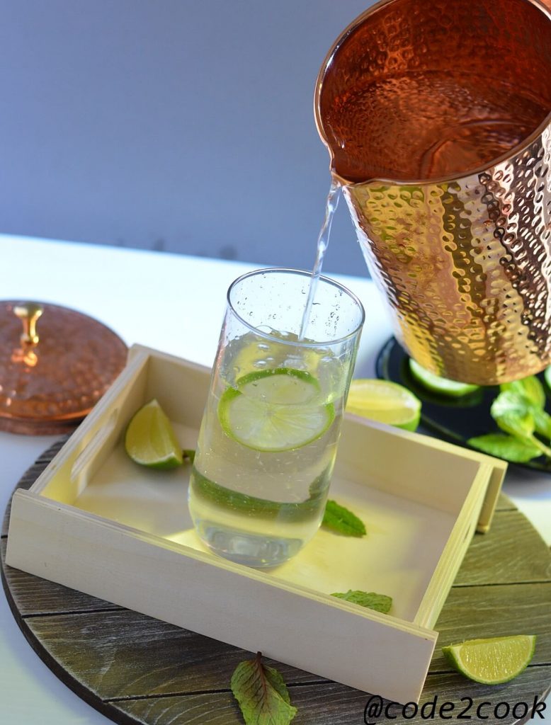 Water is poured from copper pitcher in a glass.