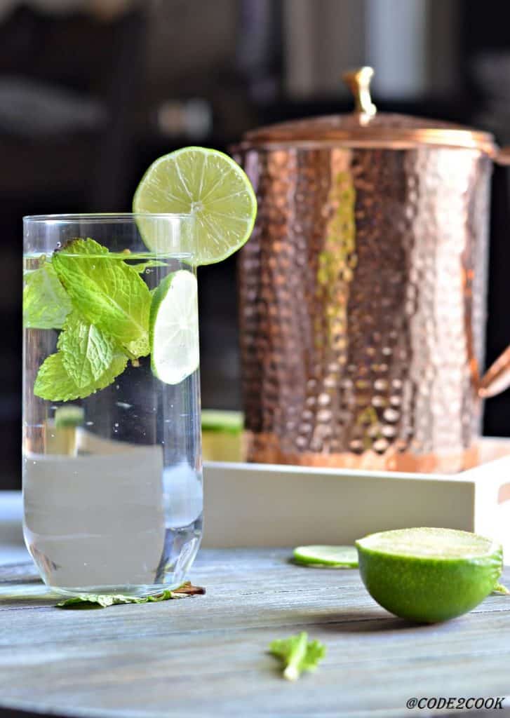 copper pitcher with a glass of drinking water served with lemon wedge & fresh mint leaves.