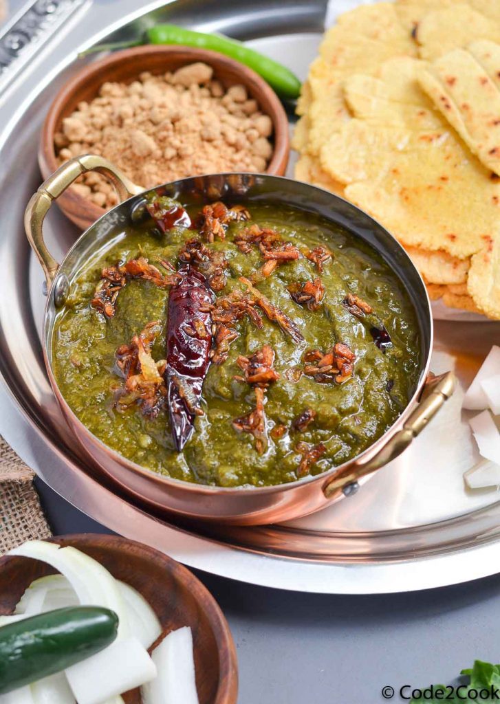 sarson ka saag served in small kadhahi along with jaggery and makki ki roti in steel serving plate.