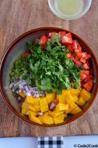 ingredients of strawberry mango salsa are in the brown bowl