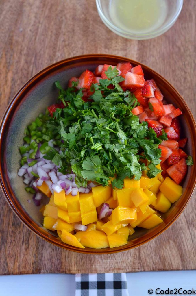 ingredients of strawberry mango salsa are in the brown bowl