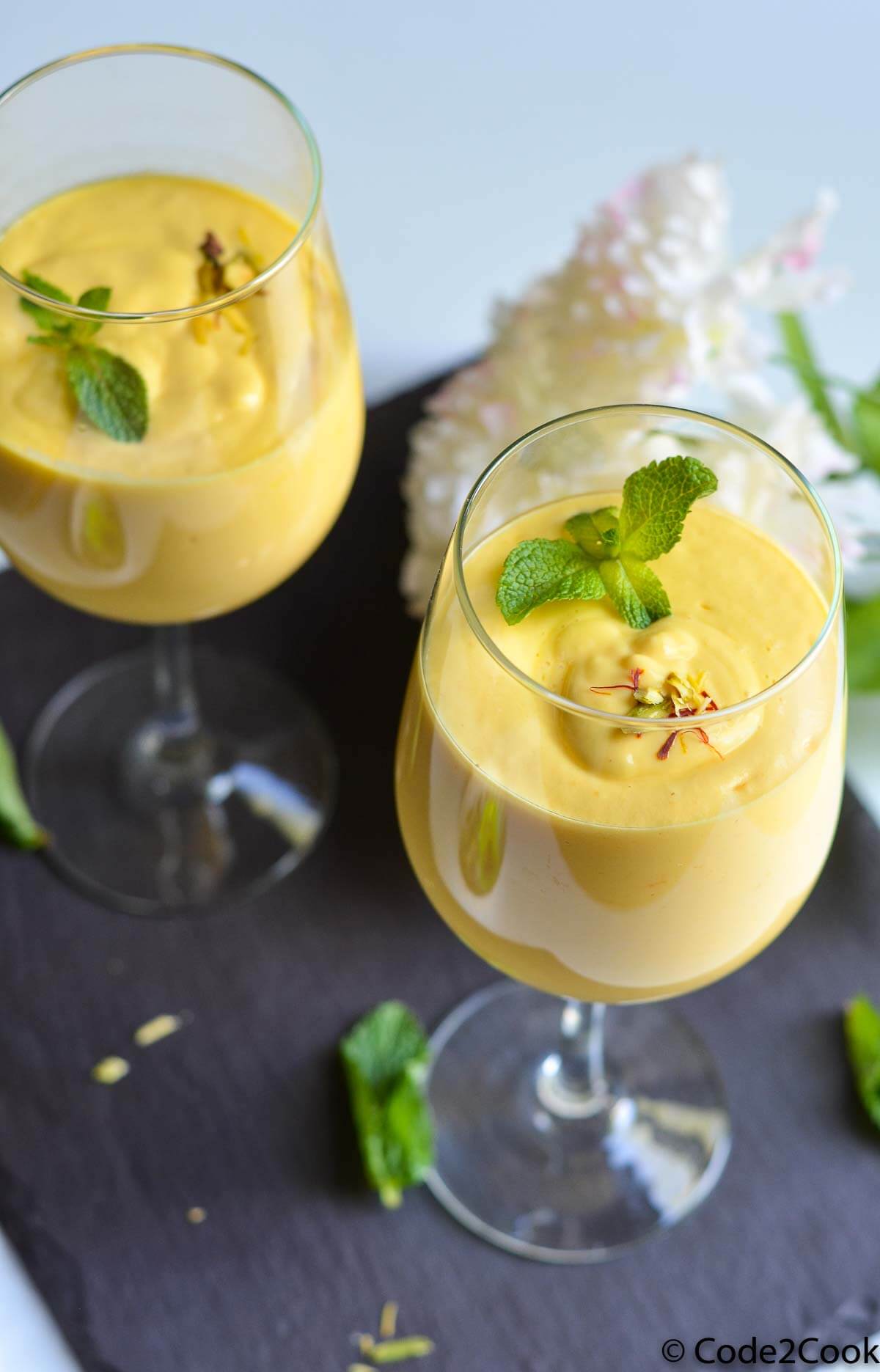 mango lassi served in tall glass and garnished with mint leaves & saffron strands.