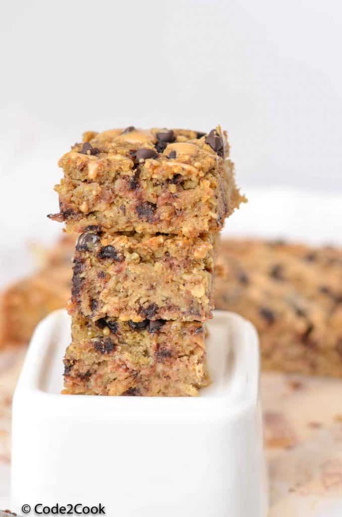 squares of oatmeal breakfast bars are stacked on while surface.