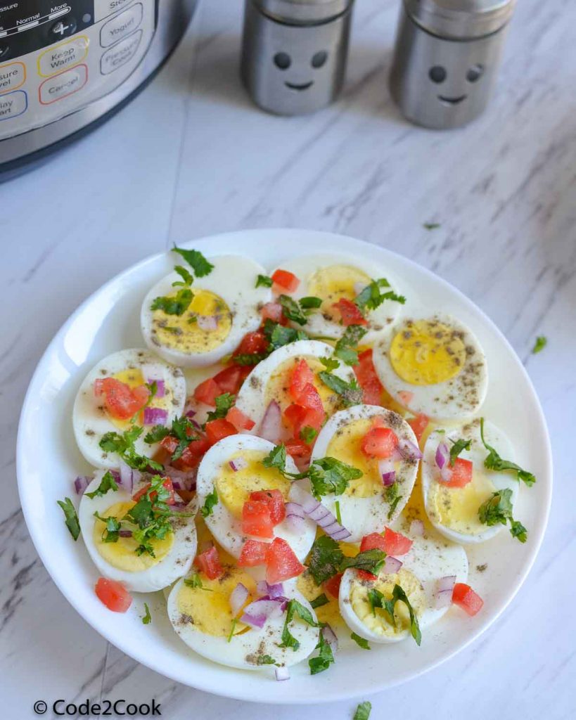 boiled eggs are served in white plate. Garnished with chopped tomato, onion and coriander. Salt & pepper sprinkled.