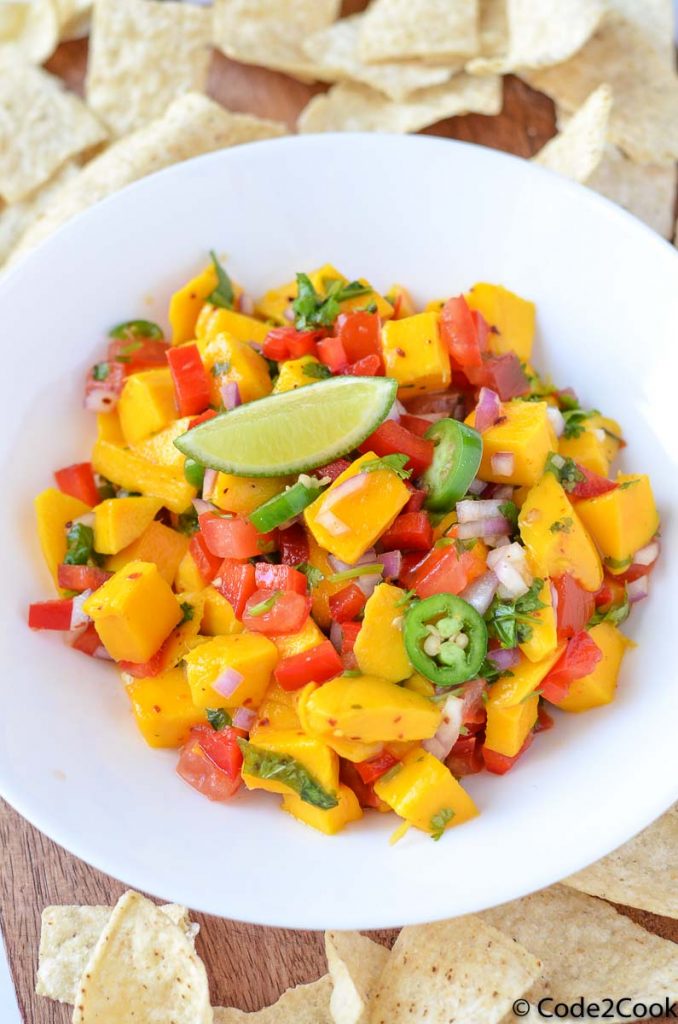 mango salsa is served in white plate garnished with lemon wedge & jalapeno.