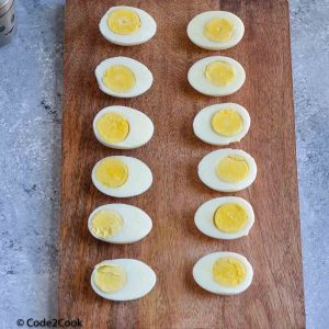 Boiled eggs cut in half and placed on wooden board. Table salt & pepper kept on left side.