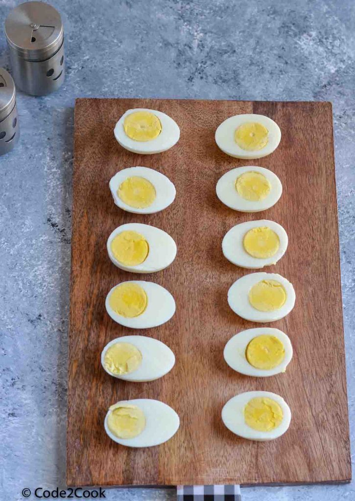 Boiled eggs cut in half and placed on wooden board. Table salt & pepper kept on left side.