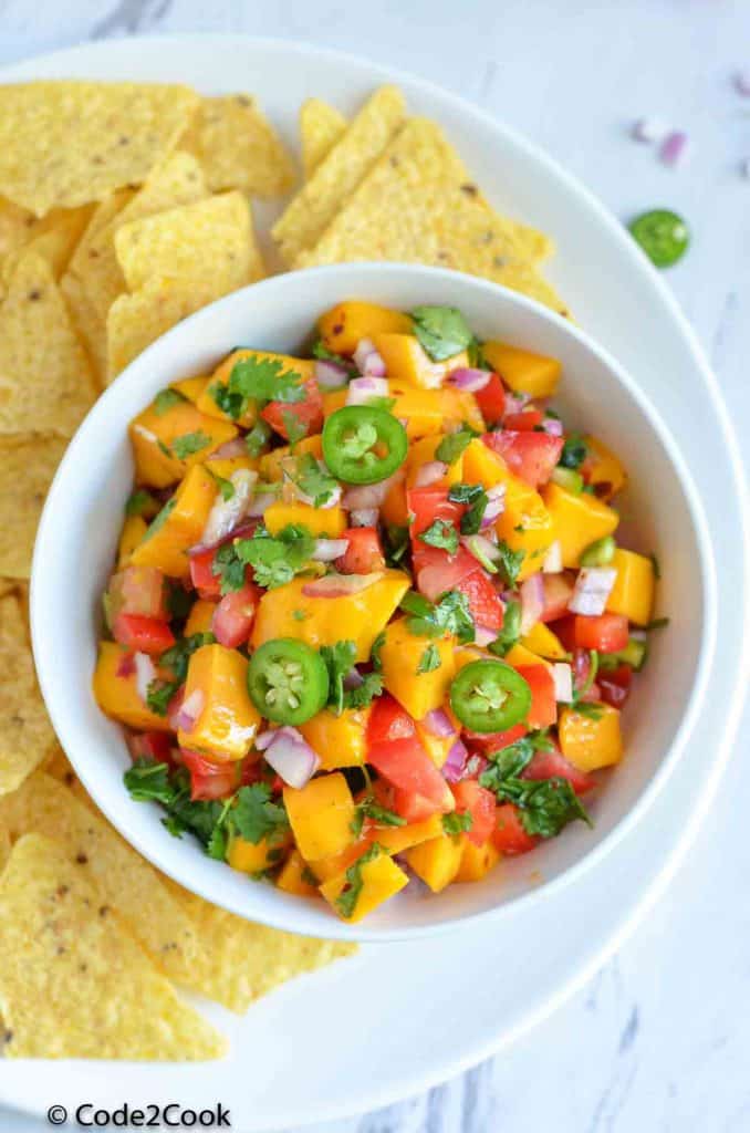 mango salsa served in white bowl with tortilla chips along side.