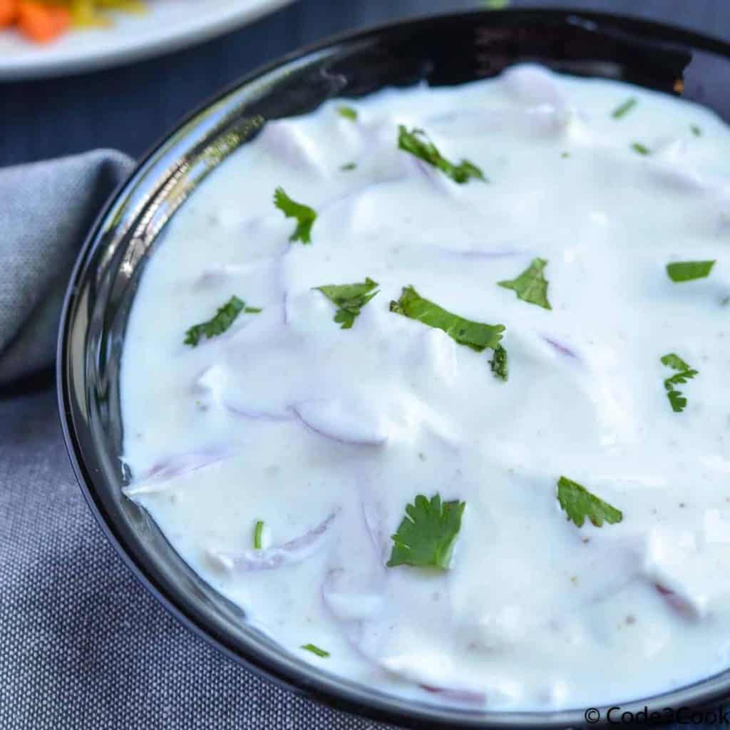 A closeup shot of onion raita served in black bowl.