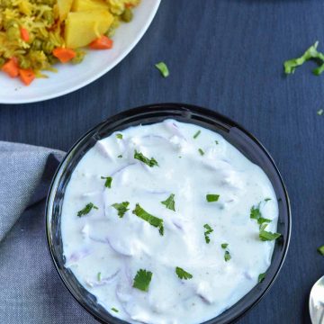 onion raita served in black bowl, garnished with green coriander. Vegetable pulao is served along with the raita.