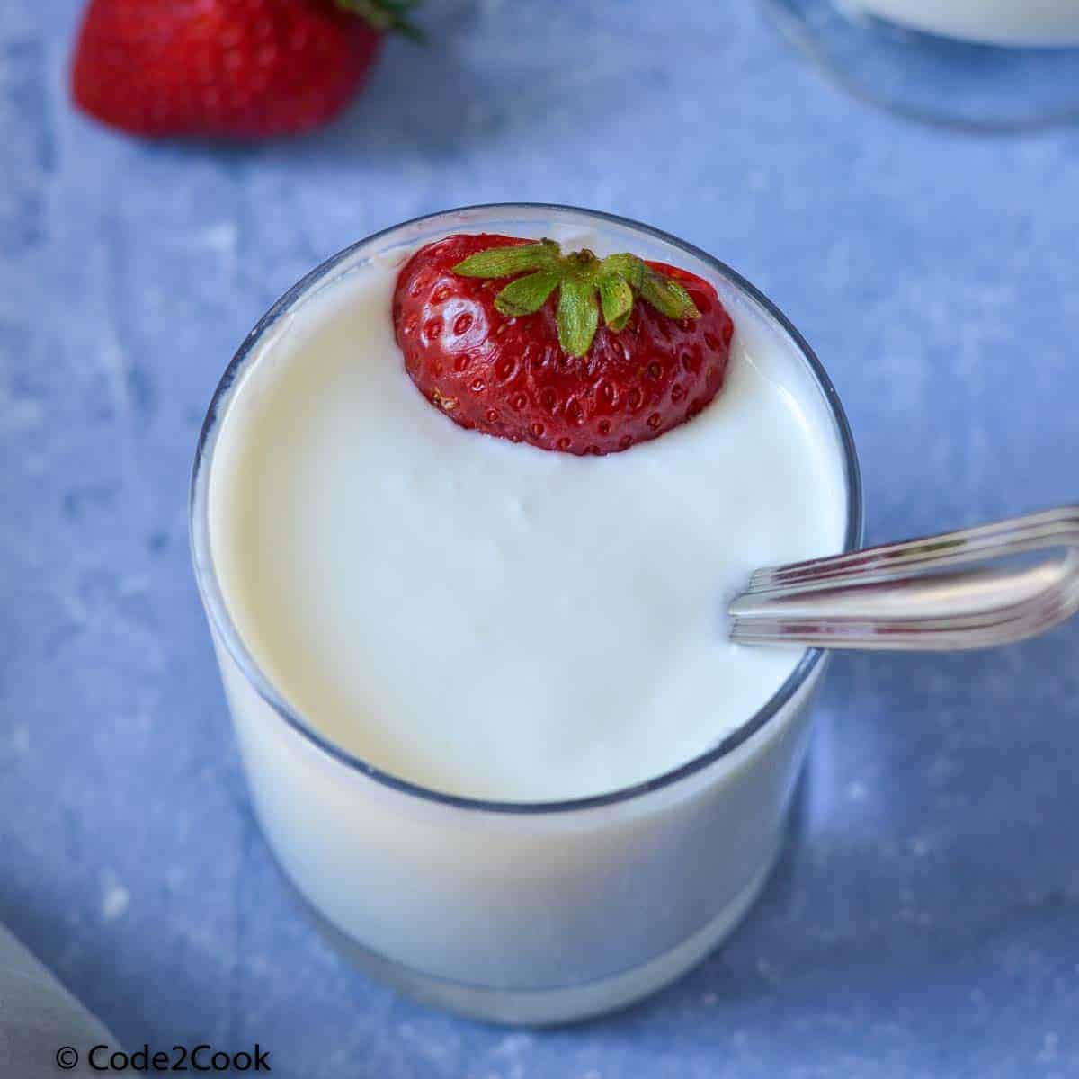 a close up shot of instant pot yogurt served in a glass with cut strawberries.