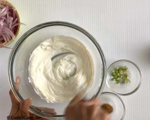 whisking yogurt with water in a glass bowl.