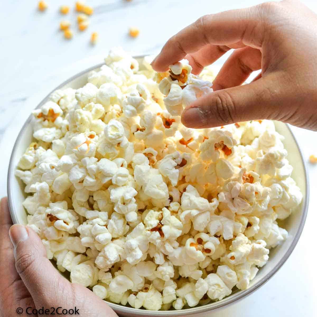 son is picking cooked popcorn from a bowl filled with them.
